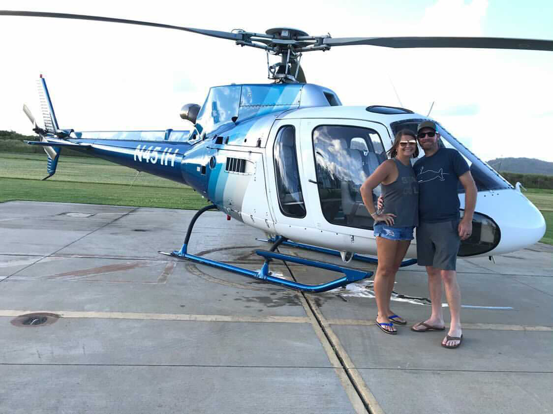 A man and woman stand proudly in front of a helicopter, showcasing their adventurous spirit with Dockshare's Xplorationer brand.