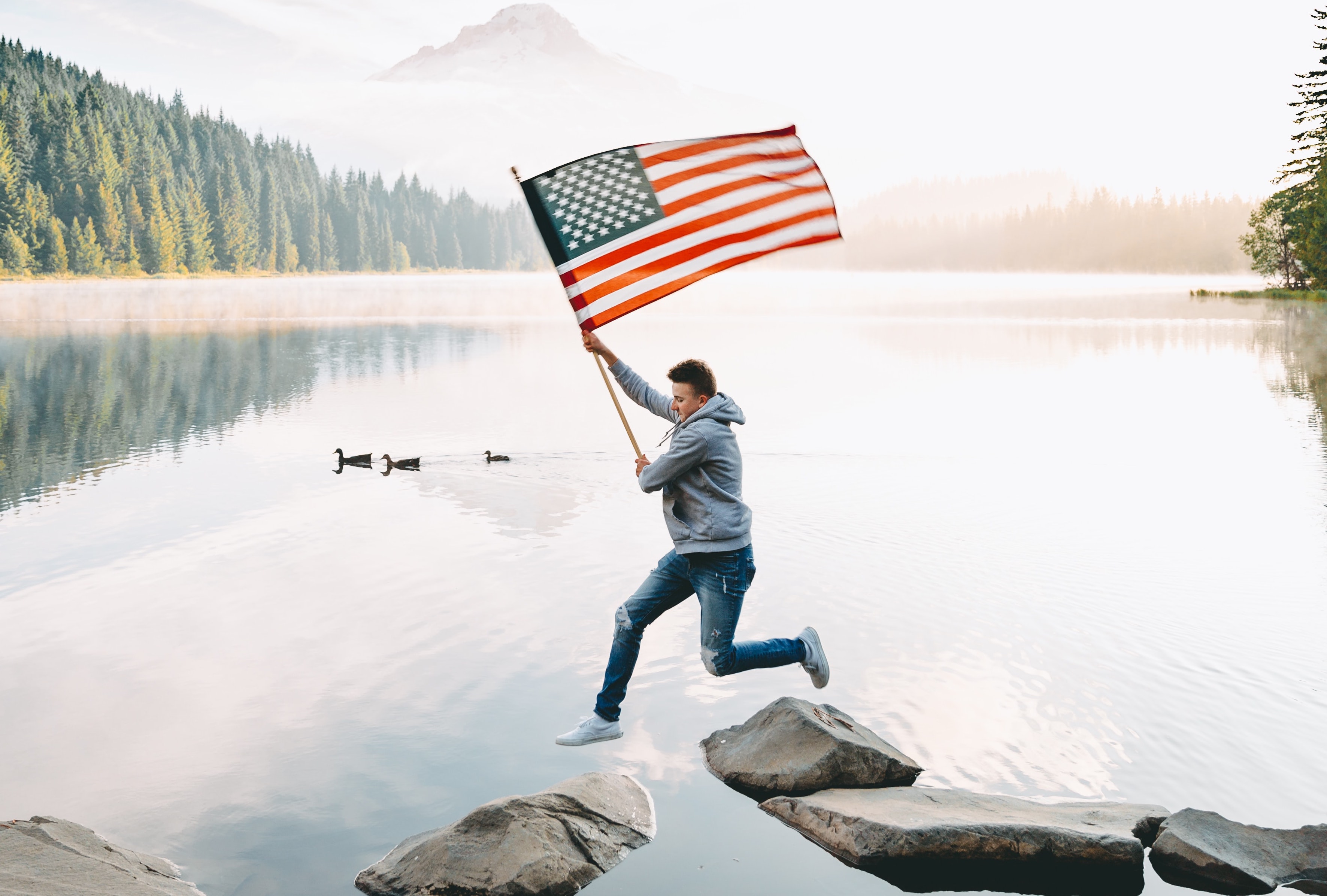 A man joyfully jumps into the water, proudly displaying an American flag, celebrating July 4th with Dockshare.