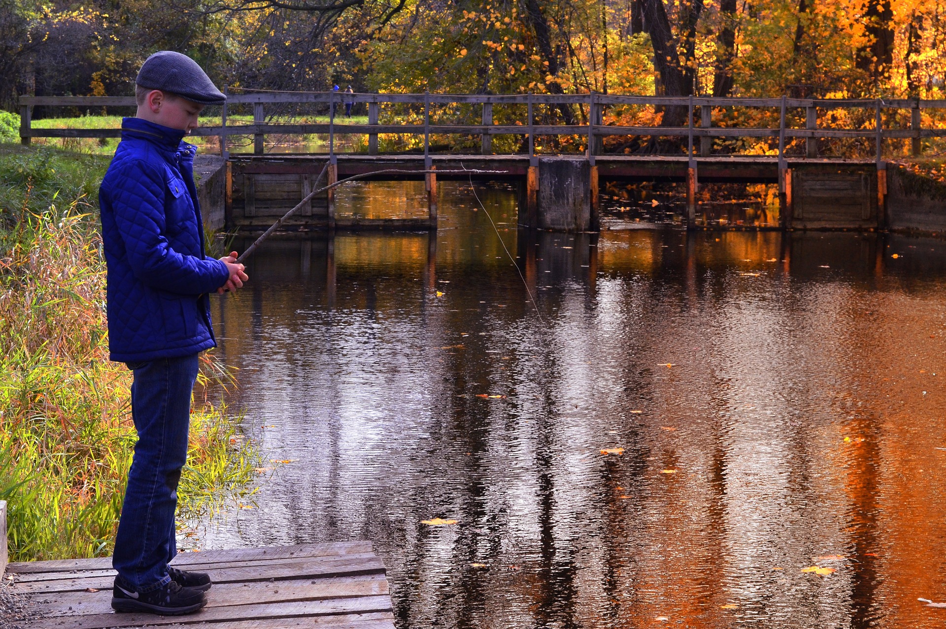 A man stands on a dock with a fishing rod, enjoying the autumn scenery. Image by Dockshare.