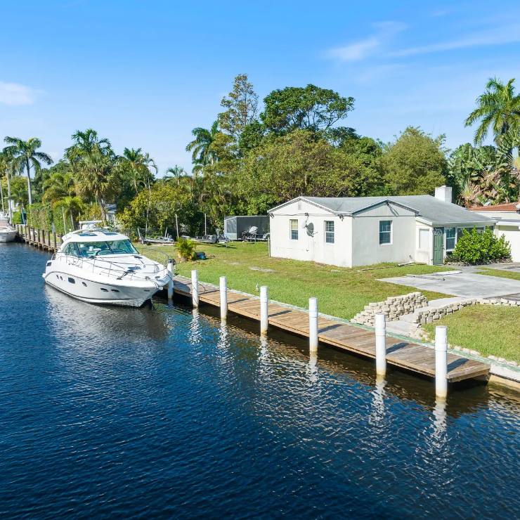 Large boat on private dock behind home in quiet residential area. Blue skies, deep blue water and vibrant green grass.