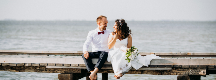 a wedding couple sits on a dock and admires each other