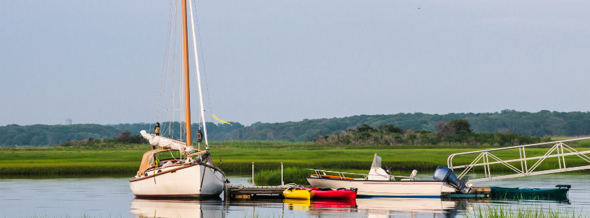 a sailboat is docked a a floating dock with salt marsh in the background