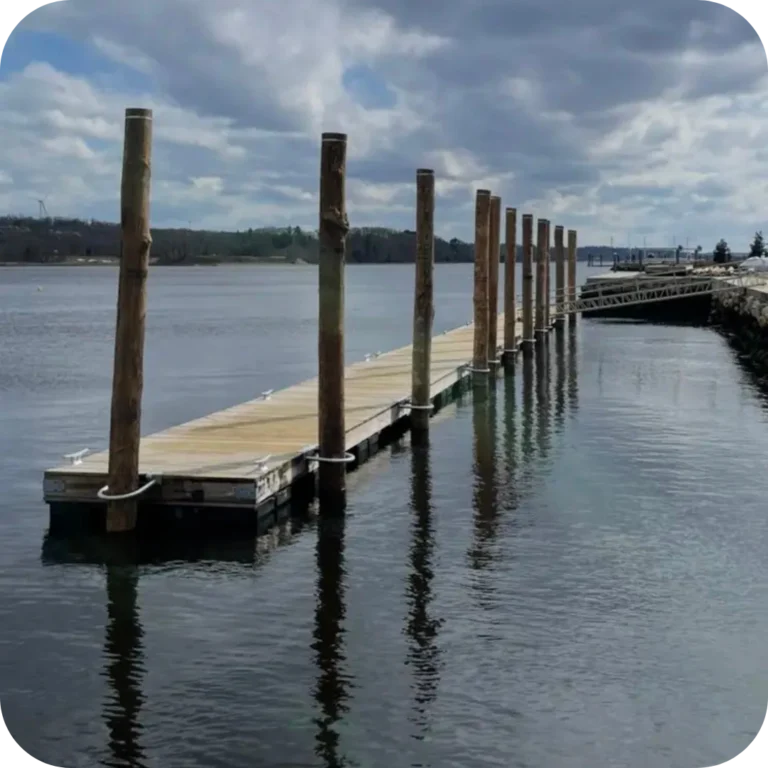 a long floating dock run parallel to the shoreline with several tall pilings around it, all against a cloudy sky