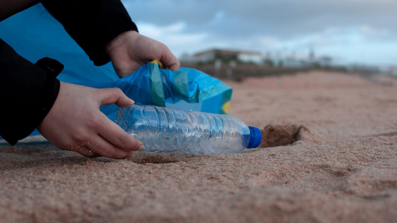 A person discards a plastic bottle into the sand, highlighting Dockshare's commitment to keeping waterways clean and beautiful.