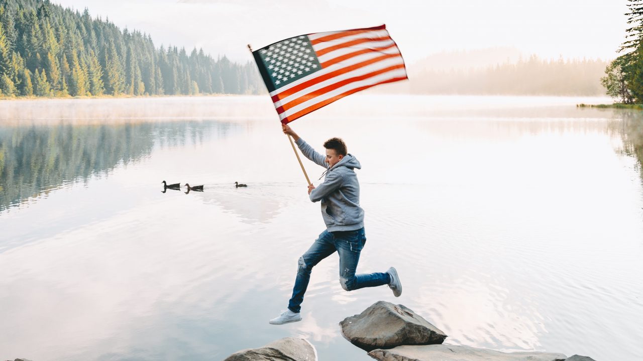A man joyfully jumps into the water, proudly displaying an American flag, celebrating July 4th with Dockshare.